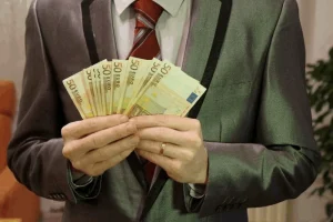 Un individuo ataviado con un sofisticado traje gris y una corbata roja vibrante cuenta meticulosamente varios billetes de 50 euros, demostrando una atenta gestión financiera.