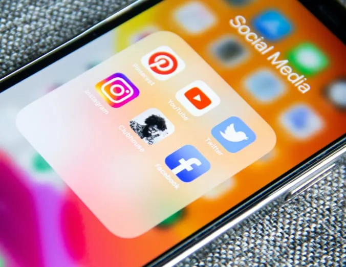 Una pantalla de teléfono inteligente muestra una carpeta denominada "Social Media", incluyendo iconos para varias plataformas de redes sociales, tales como Instagram, Pinterest, YouTube, Twitter y Facebook. Esta imagen optimiza el uso correcto de palabras clave importantes para mejorar el posicionamiento SEO. Se referencian destacadas plataformas digitales que son tendencia en búsquedas online y crucialmente relevantes para la estrategia SEO en marketing digital.